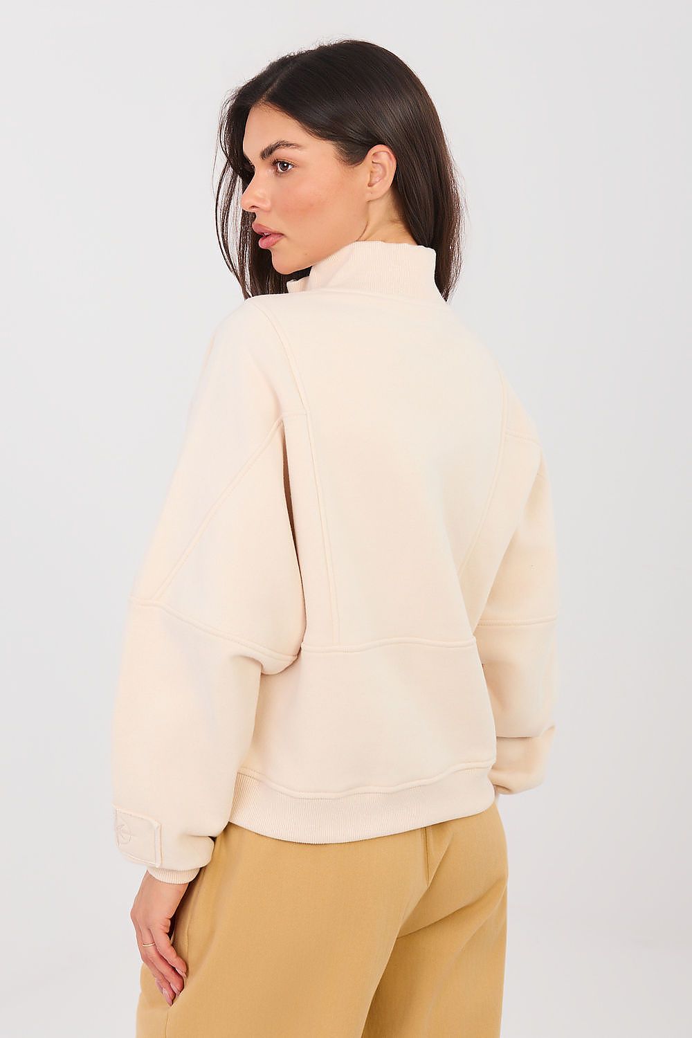 Woman wearing a cream-colored jacket and beige pants on a white background