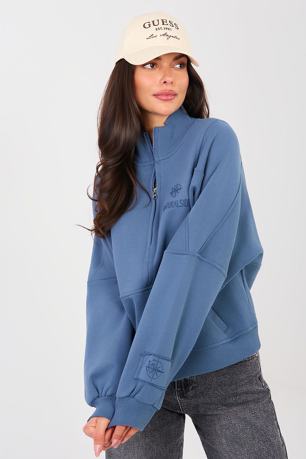 Woman wearing a blue Guess sweatshirt and beige cap on a white background