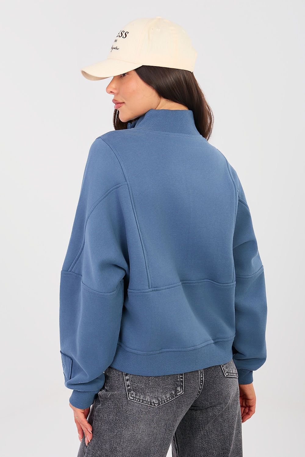 Person wearing a blue sweatshirt and beige cap on a white background