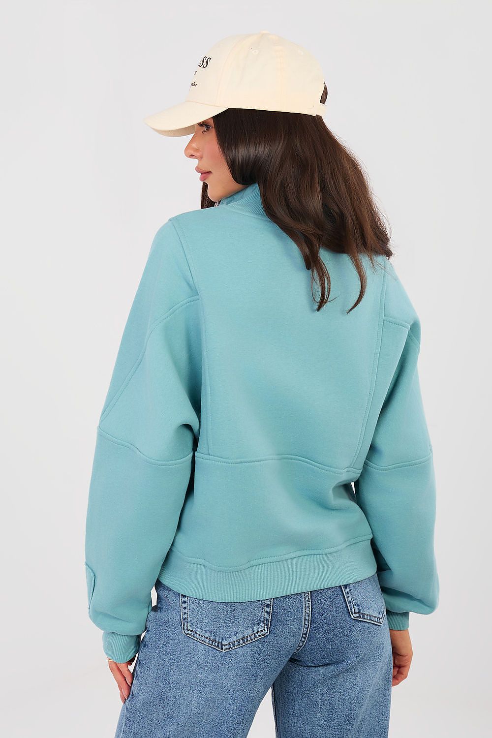 Person wearing a teal sweatshirt and beige cap on a plain background