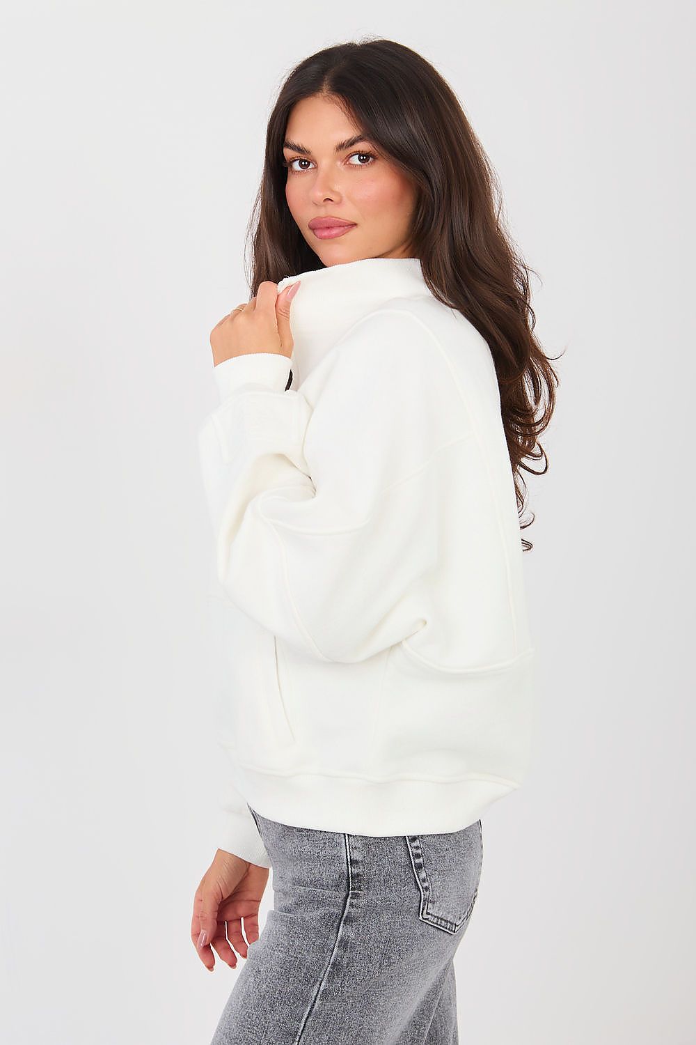Woman wearing a white sweater and gray jeans on a white background