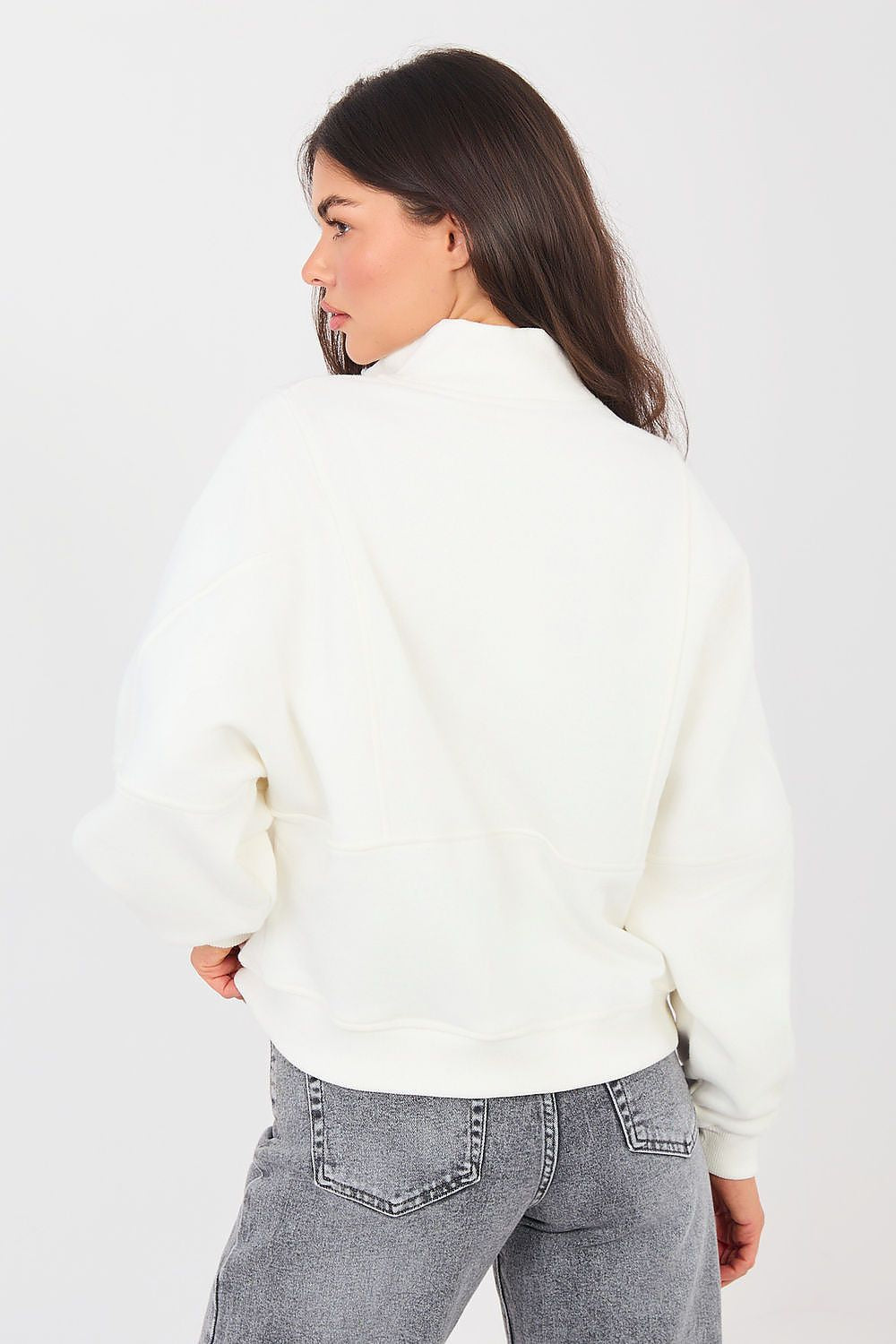 Woman wearing a white sweater and gray jeans against a plain background