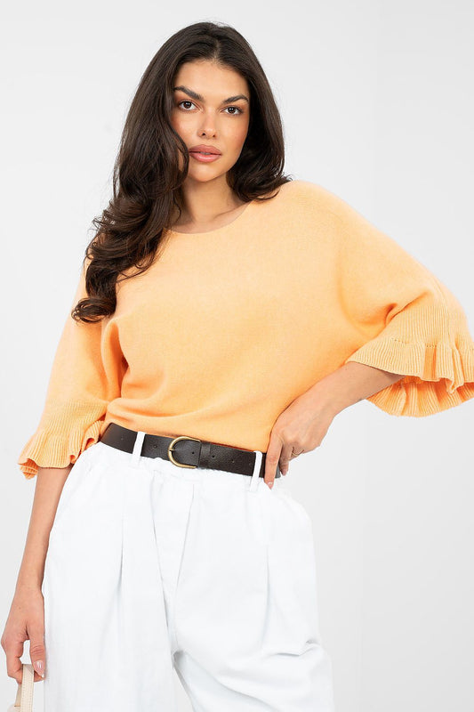 Woman wearing an orange blouse with ruffled sleeves and white pants on a white background