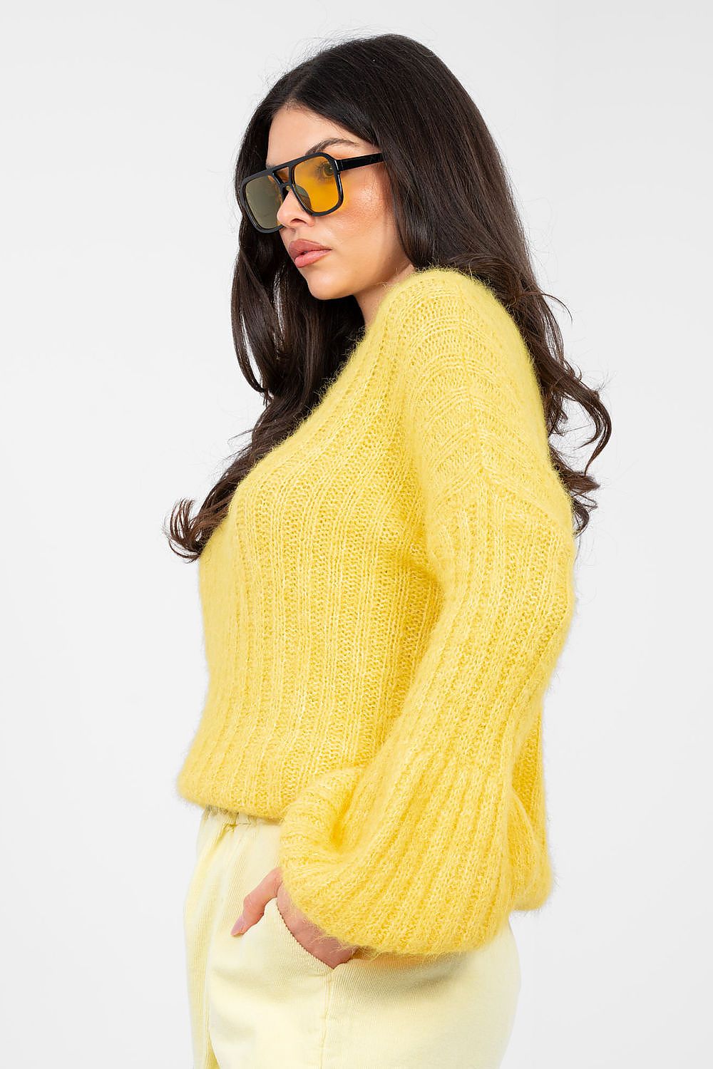 Woman wearing a yellow sweater and sunglasses on a white background