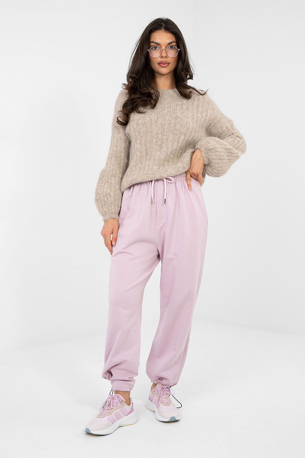 Woman wearing a beige sweater and pink pants on a white background