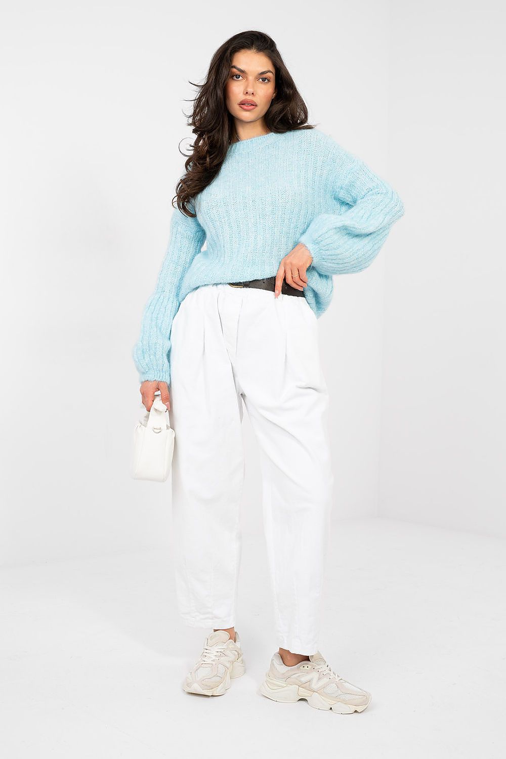 Woman wearing a light blue sweater and white pants on a white background
