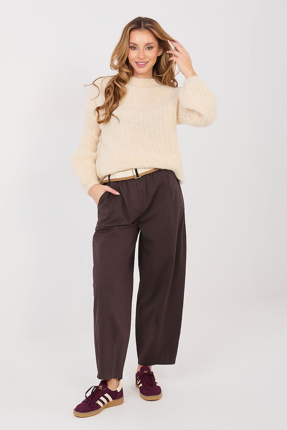 Woman wearing a beige sweater and brown pants on a white background