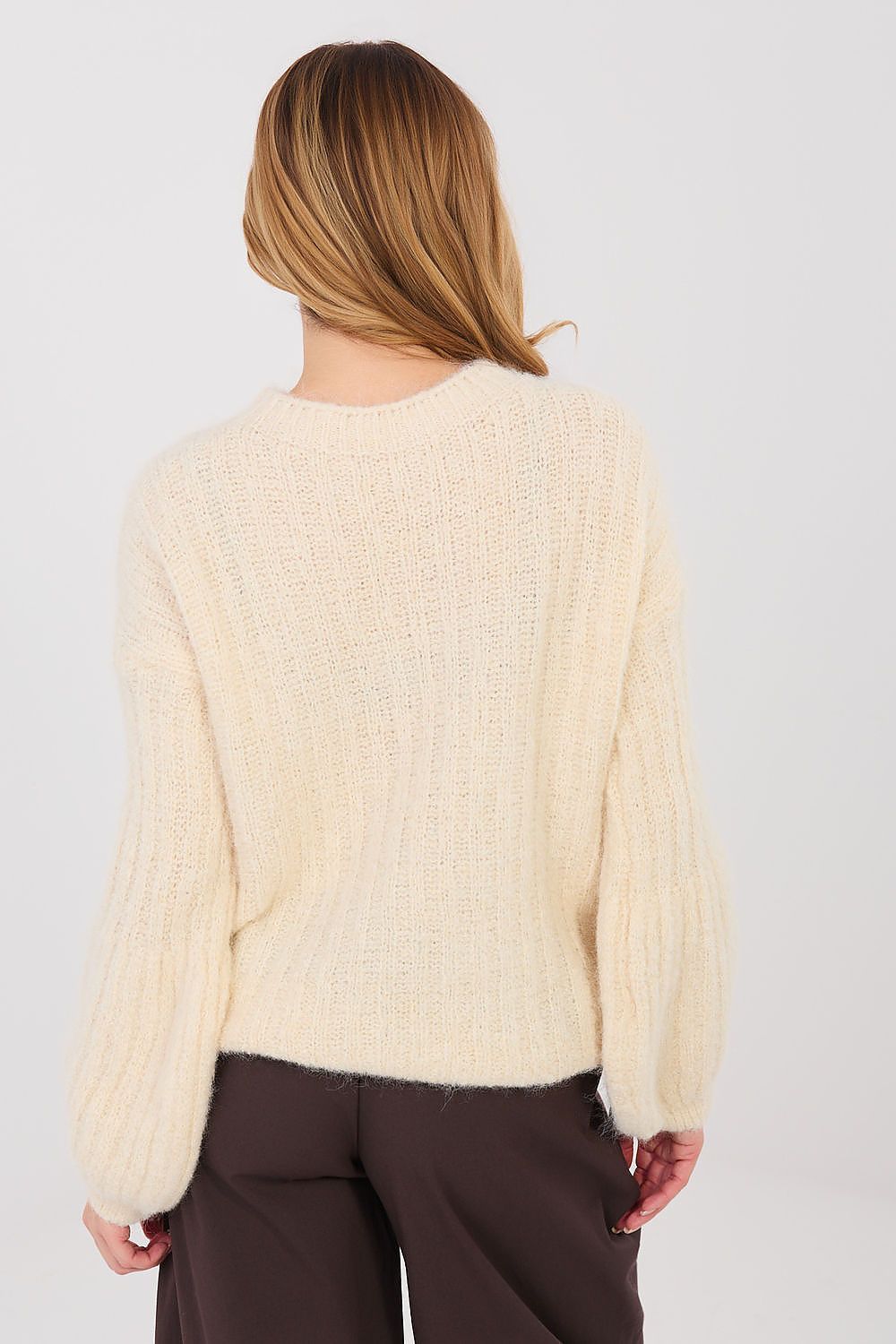 Person wearing a cream sweater and brown pants on a plain background