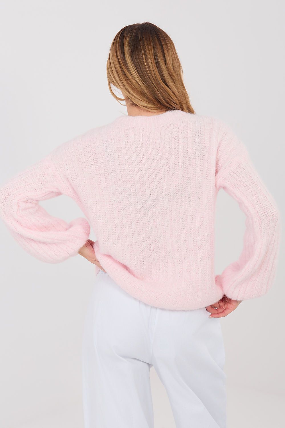 Person wearing a light pink sweater and light gray pants on a white background
