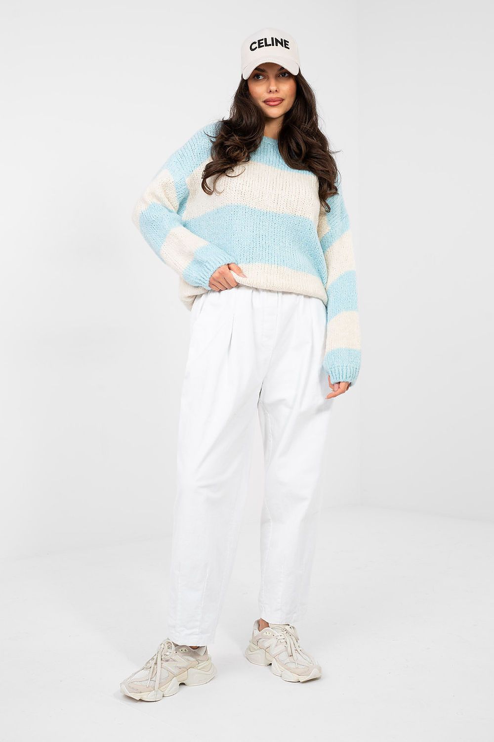 Person wearing a striped sweater and white pants with a white background