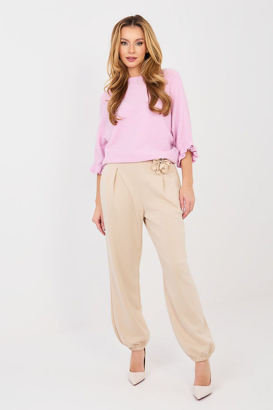 Woman wearing a pink sweater and beige pants on a white background