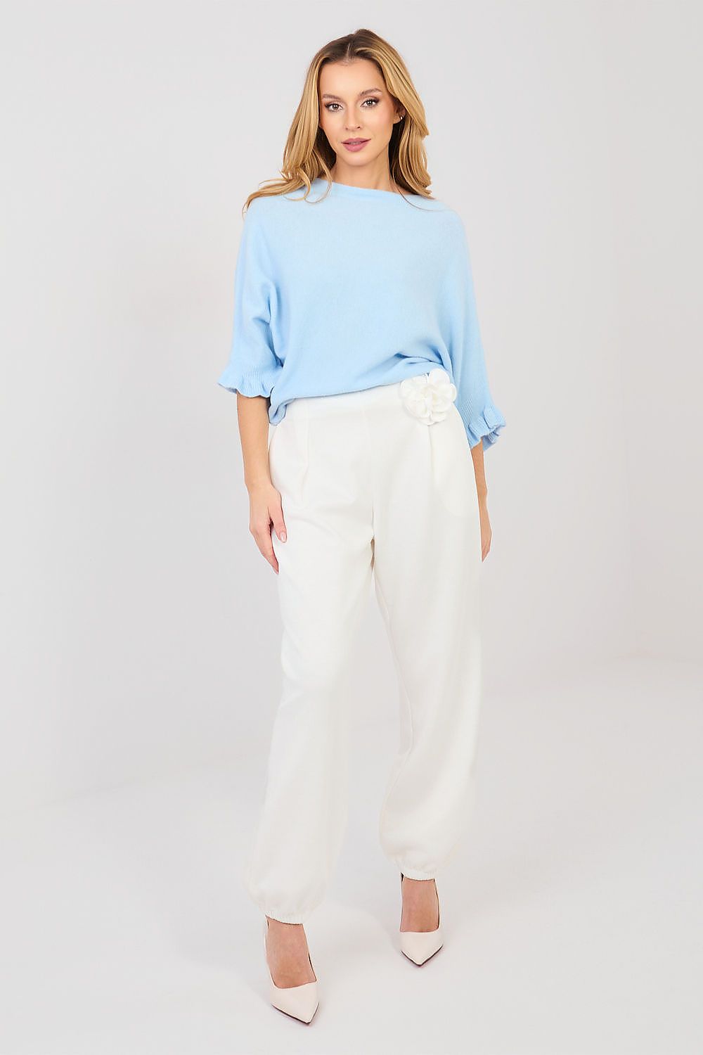 Woman wearing a light blue top and white pants on a plain background