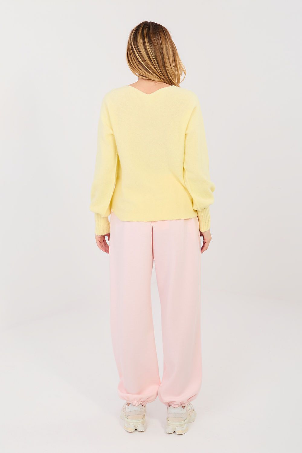 Person wearing a yellow sweater and pink pants on a white background