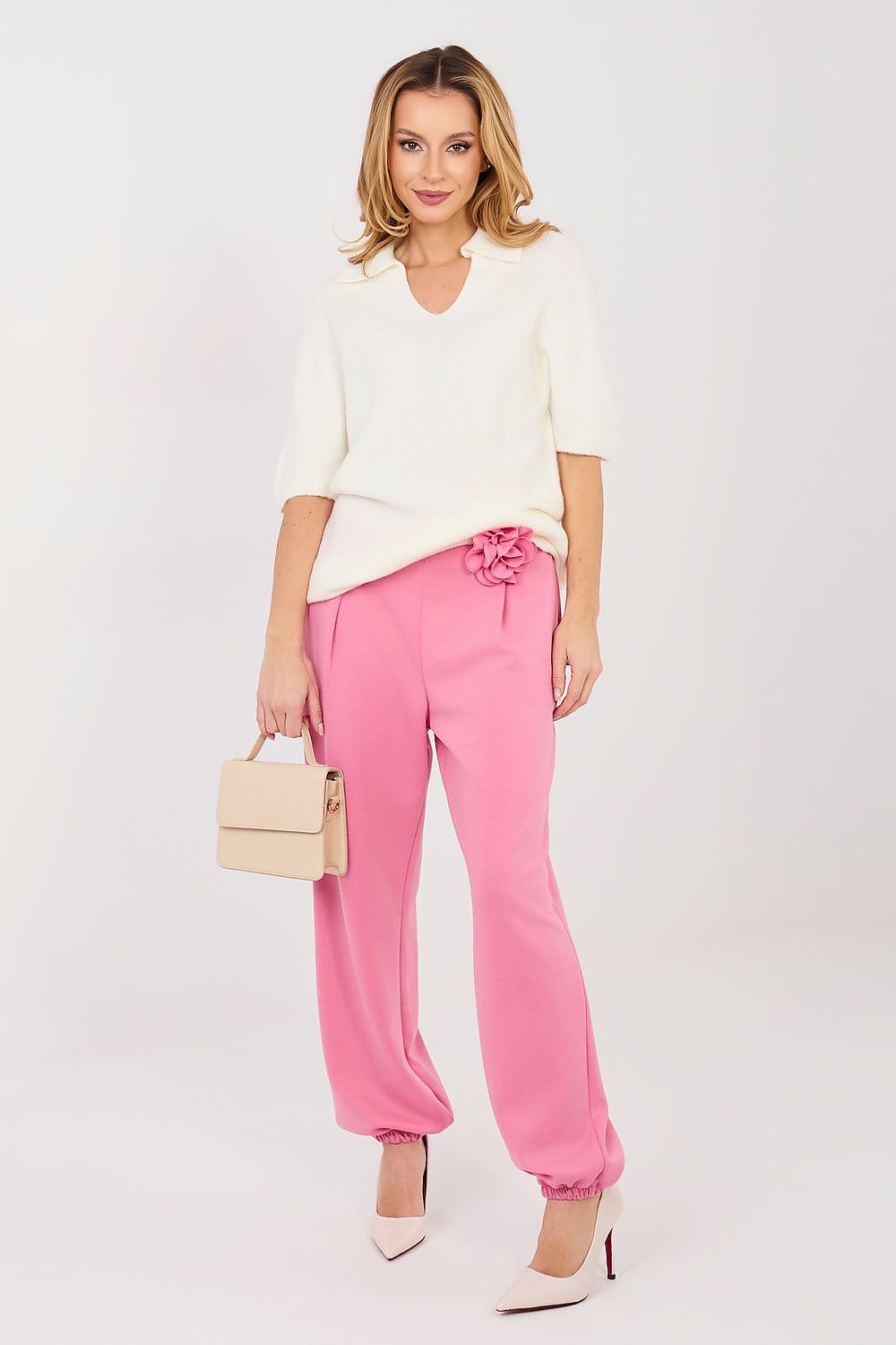 Woman wearing a white top and pink pants with a beige handbag on a white background