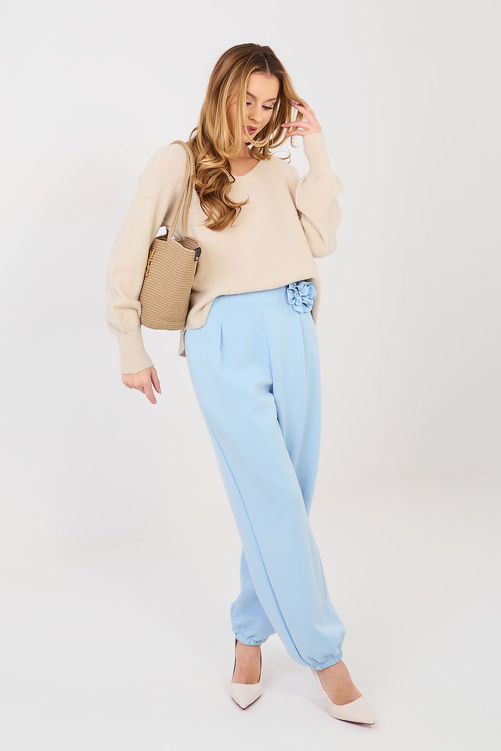 Woman wearing a beige sweater and light blue pants with a beige handbag on a white background