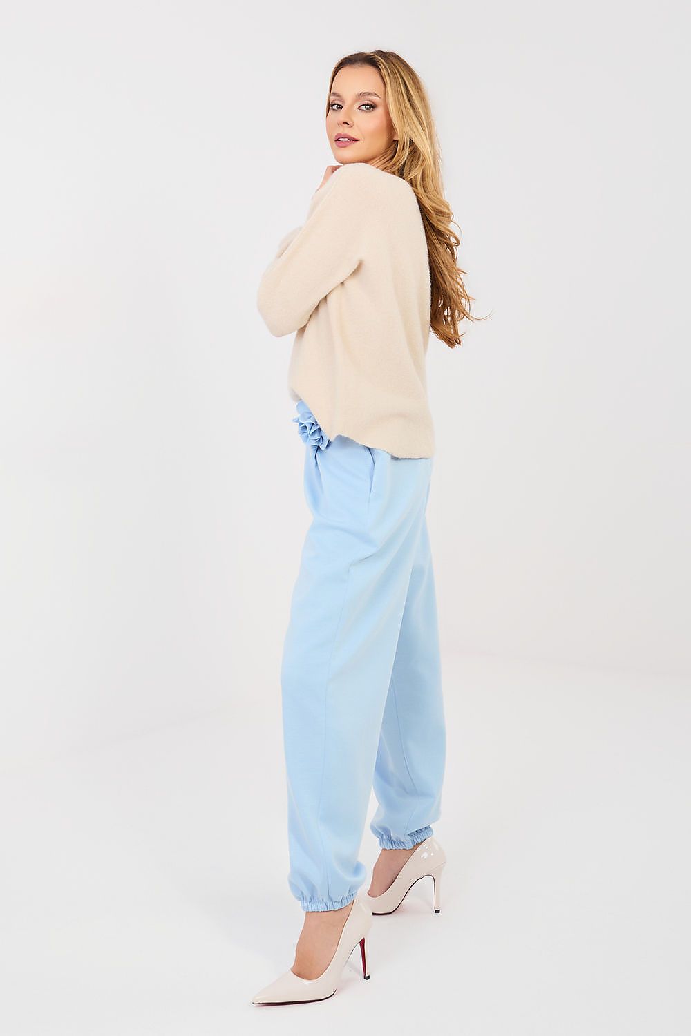 Woman wearing a beige sweater and light blue jeans on a white background