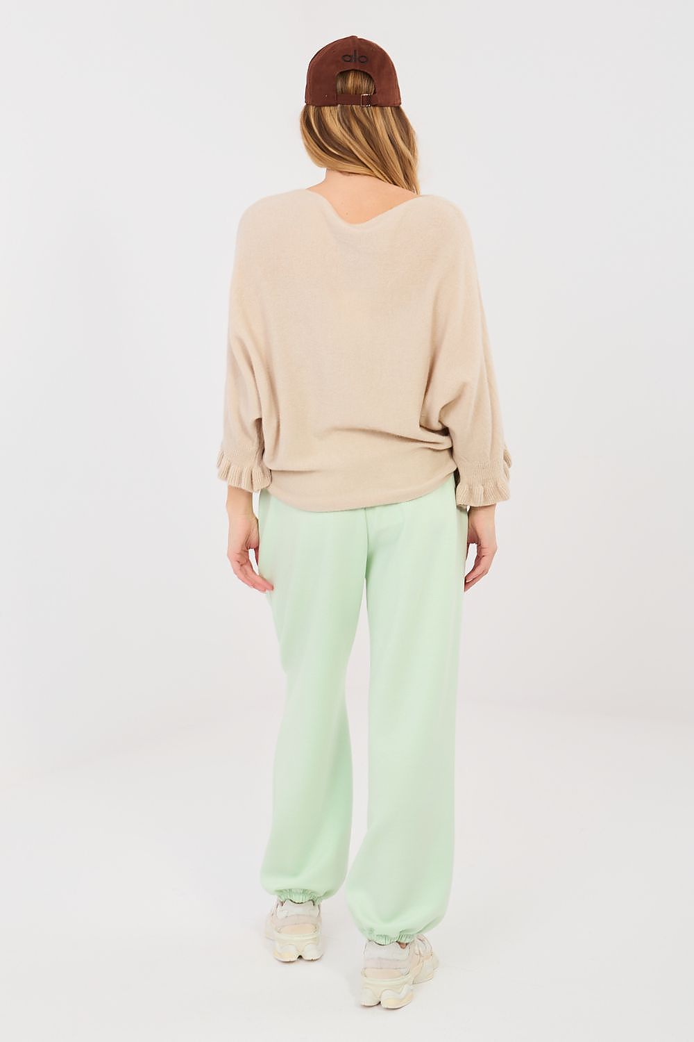 Person wearing a beige top and light green pants on a white background