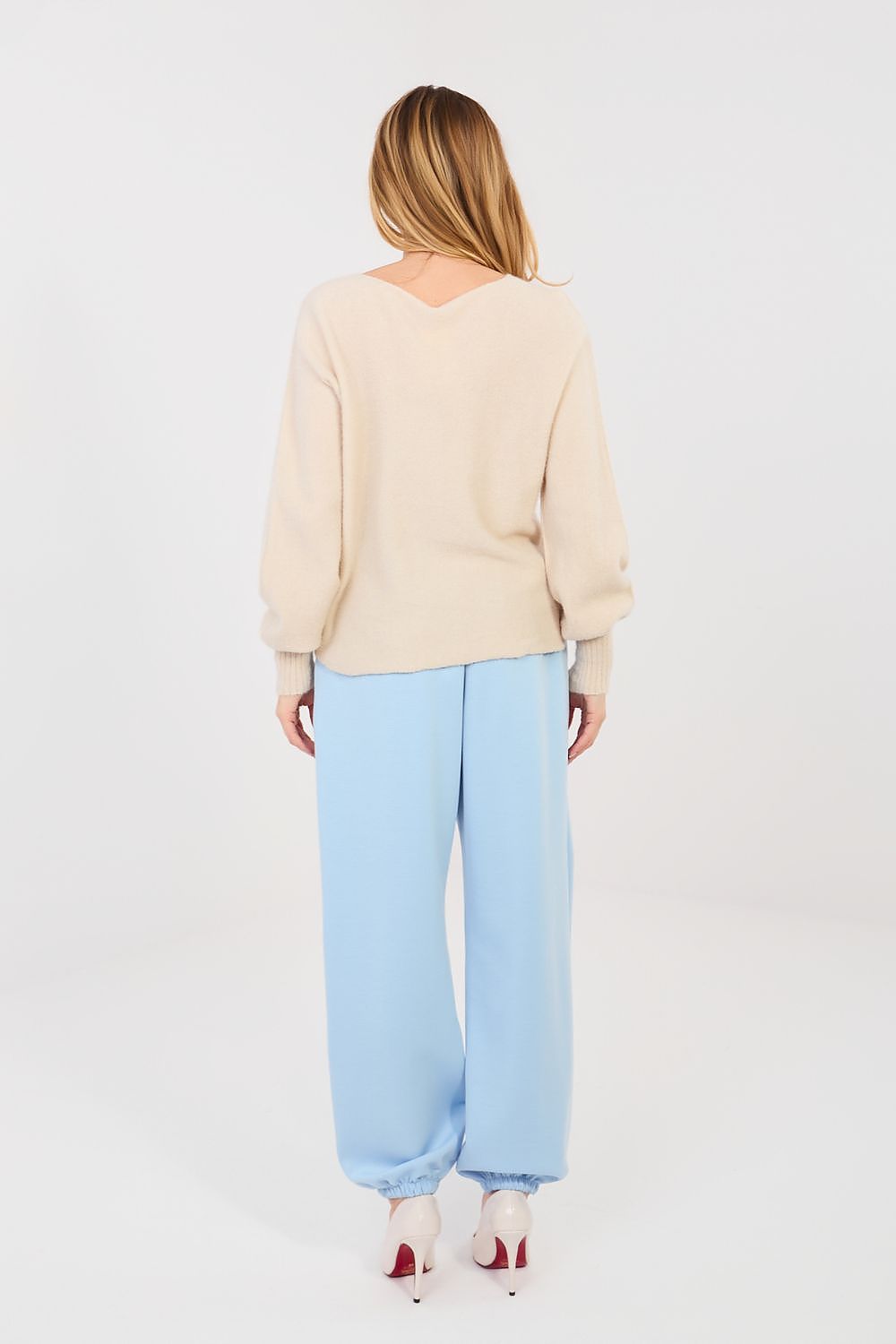 Woman wearing a beige sweater and light blue pants on a white background