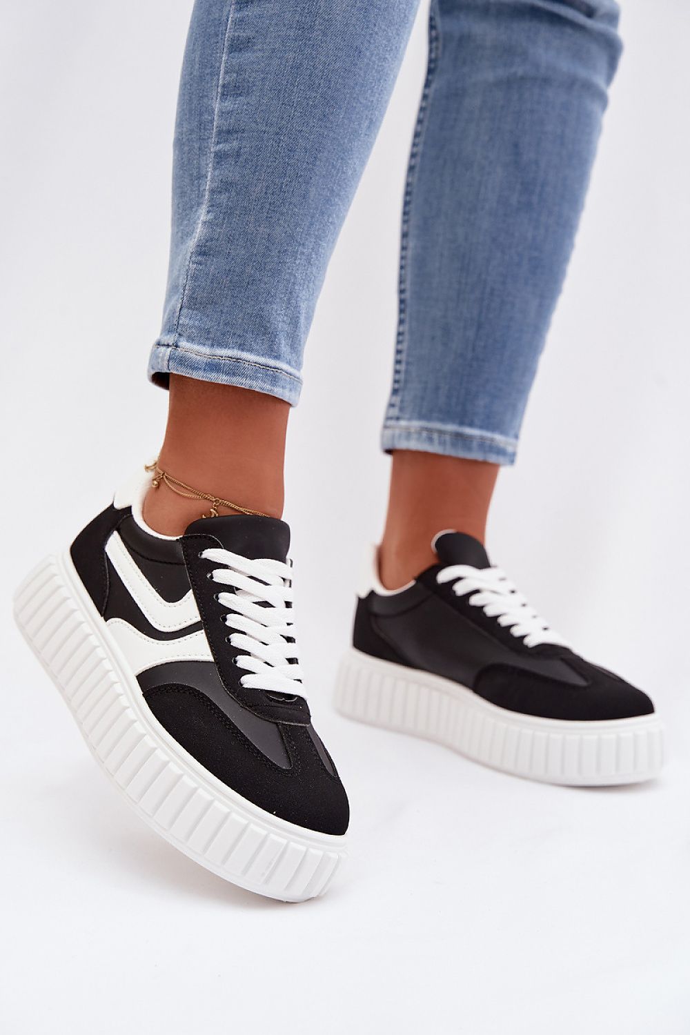 Black and white sneakers worn with blue jeans on a white background