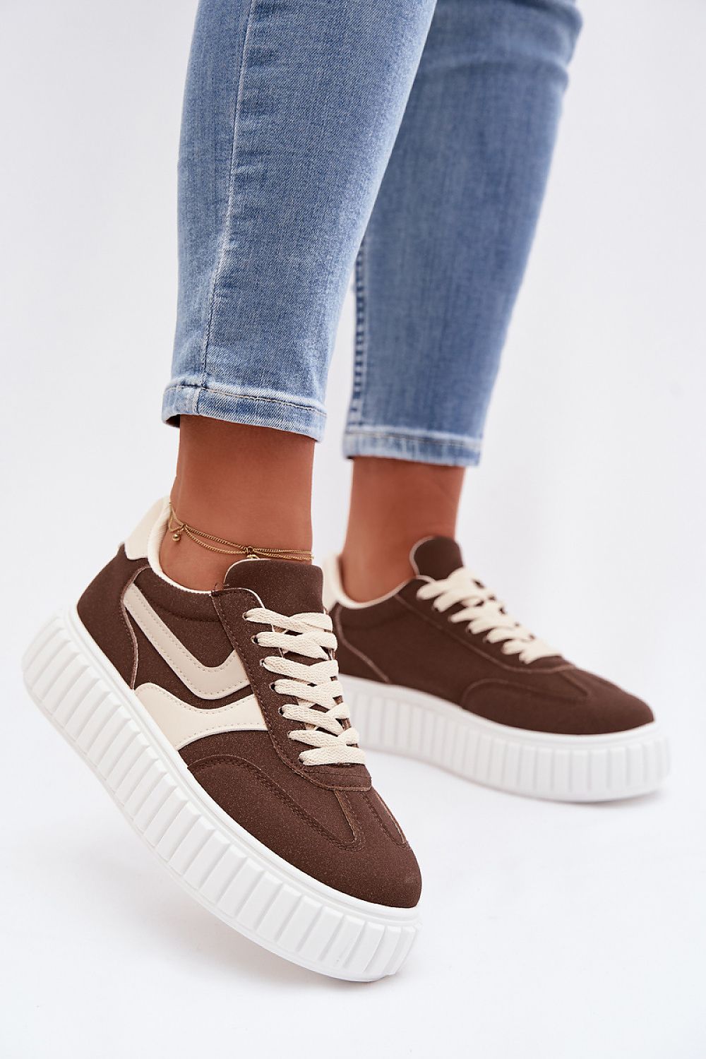 Brown sneakers with white accents worn with blue jeans on a light background