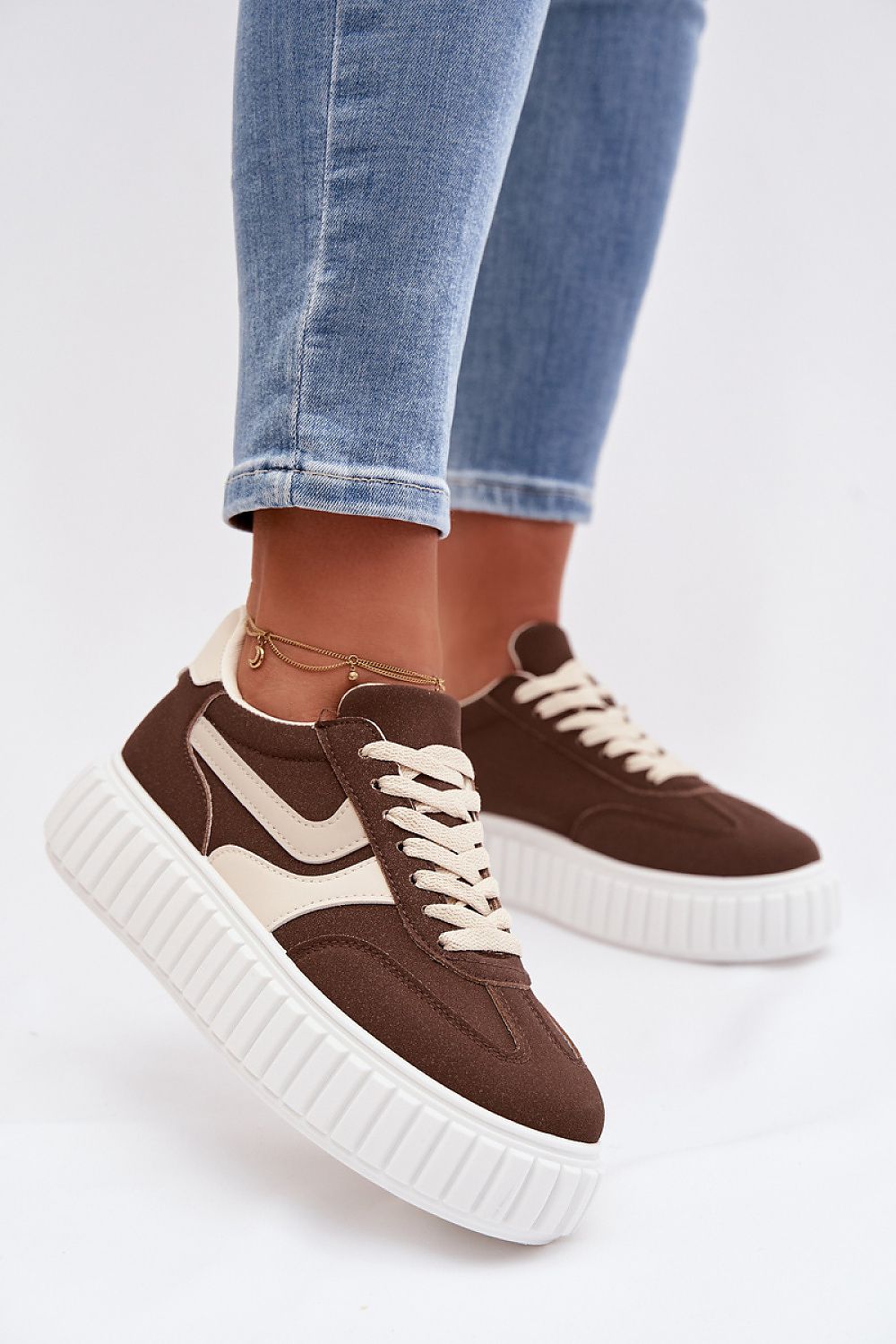 Brown sneakers with white soles worn with blue jeans on a light gray background
