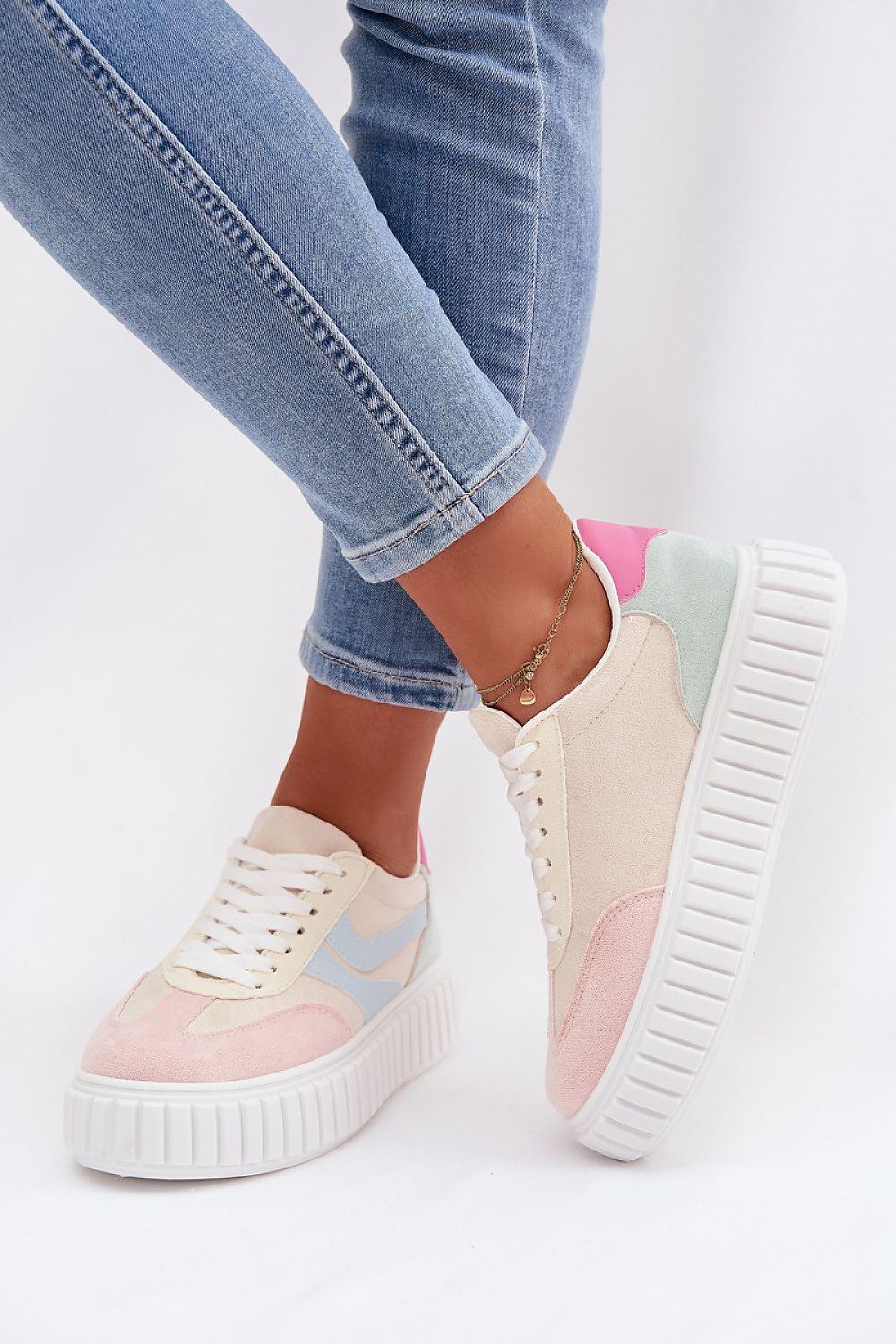 Pastel-colored sneakers with a thick sole worn with light blue jeans on a white background