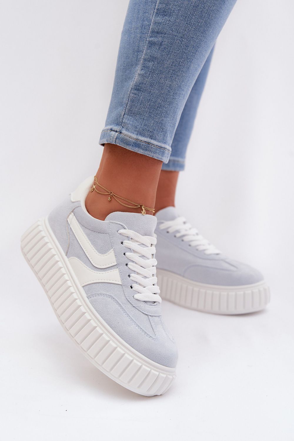 Light blue sneakers with white soles worn with light blue jeans on a white background