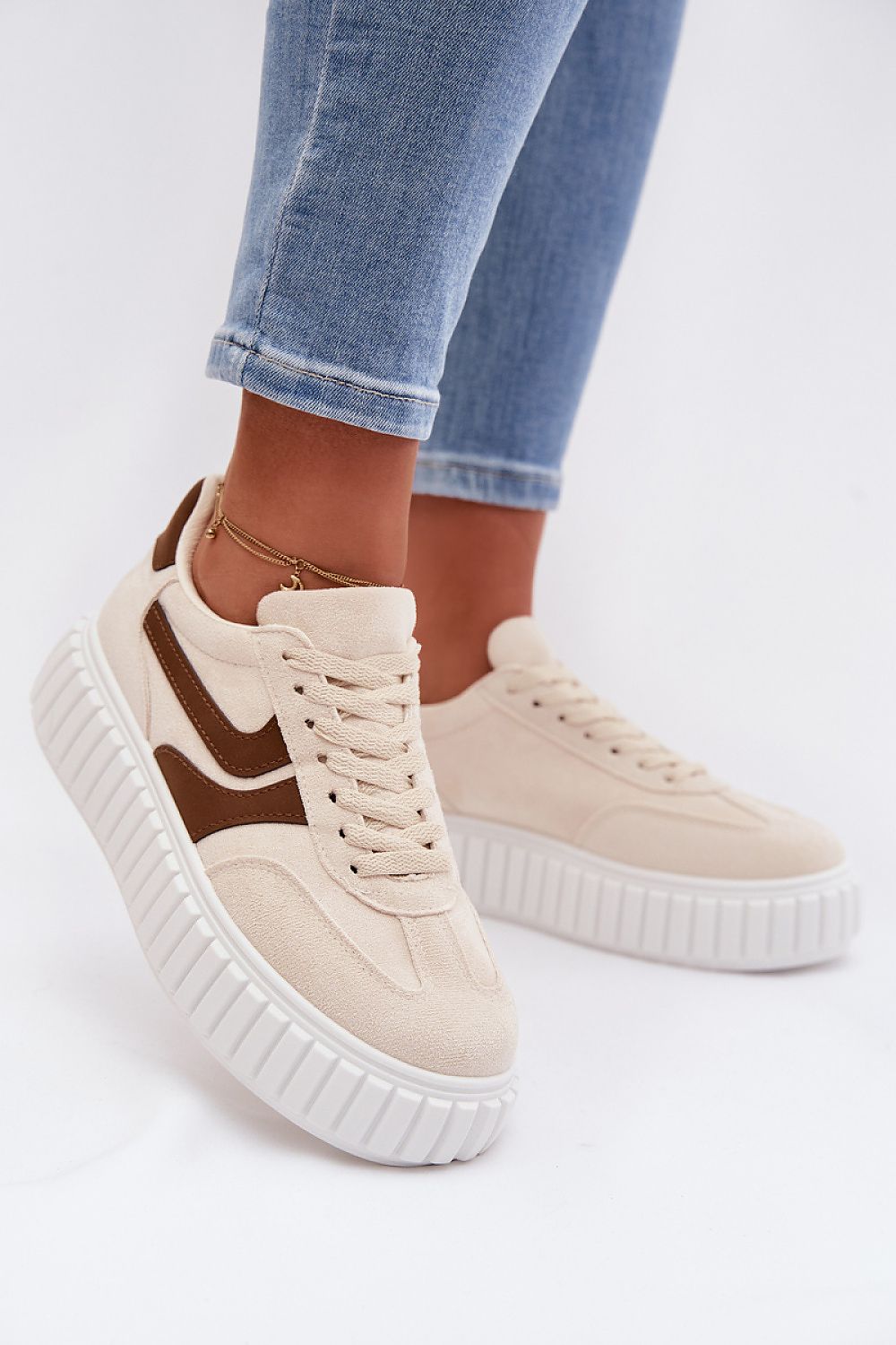 Beige sneakers with brown accents worn with light blue jeans on a white background