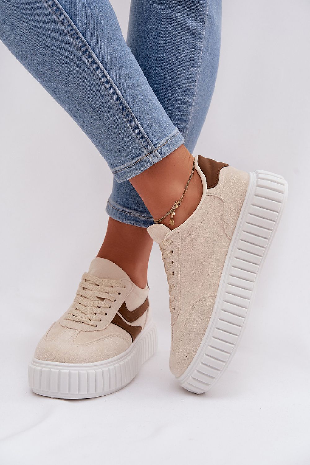 Beige sneakers with white soles worn with blue jeans on a light gray background