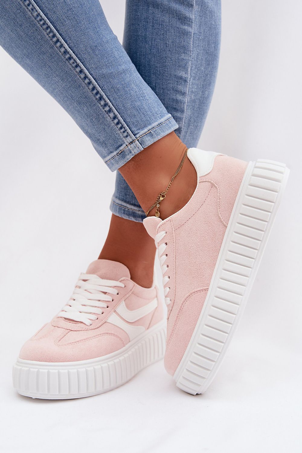 Pink sneakers with white soles worn with blue jeans on a light background