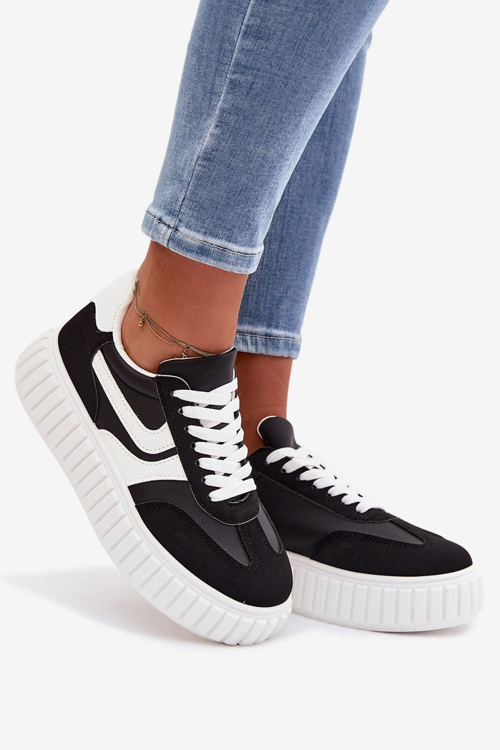 Black and white sneakers worn with blue jeans on a white background