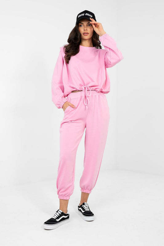 Person wearing a pink tracksuit and black sneakers on a white background