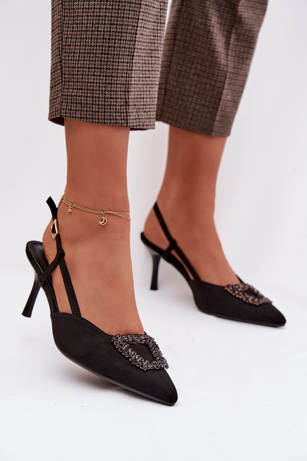 Black high-heeled shoes with embellishments worn by a person on a white background