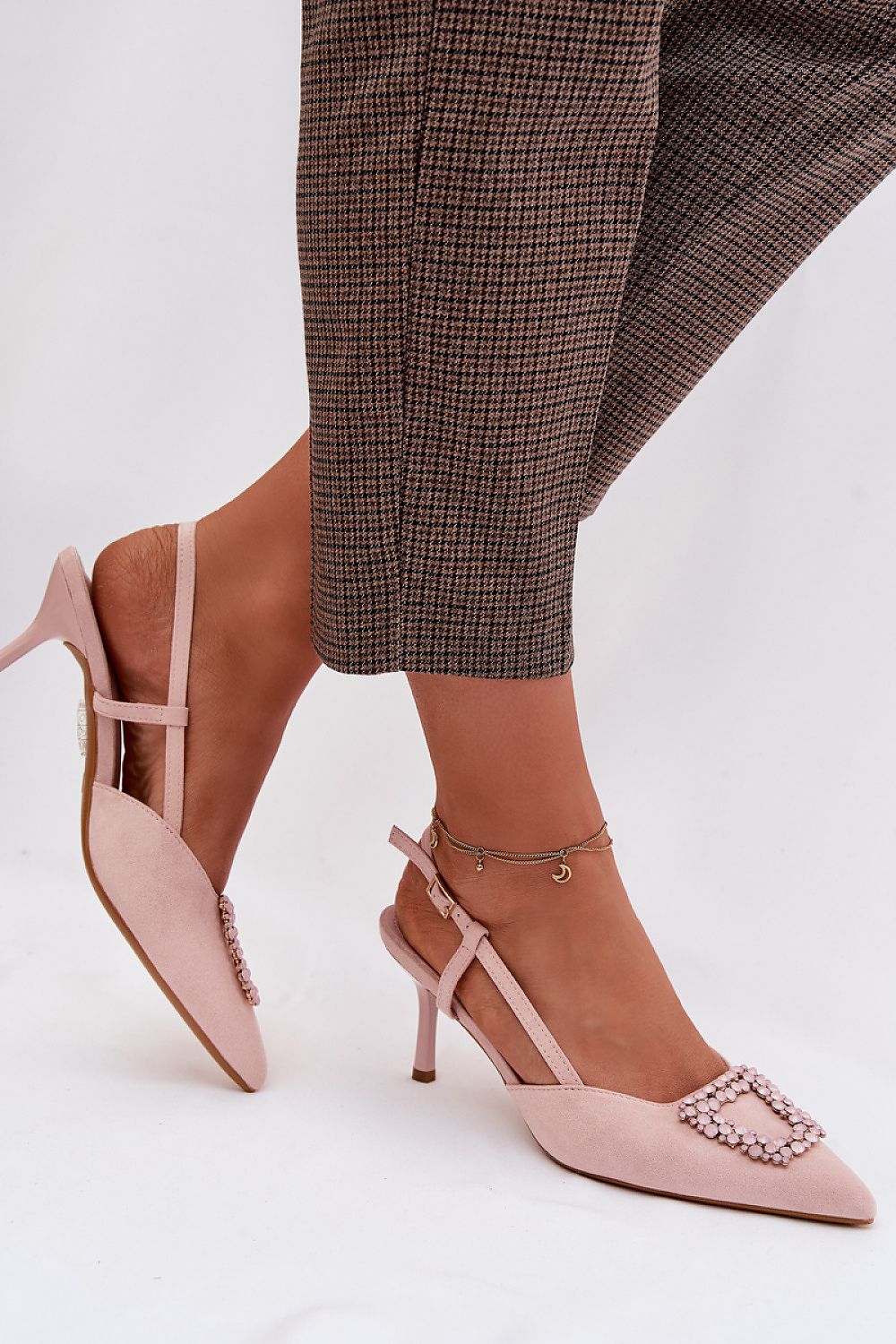 Pink high-heeled shoes with embellishments worn with plaid pants on a white background