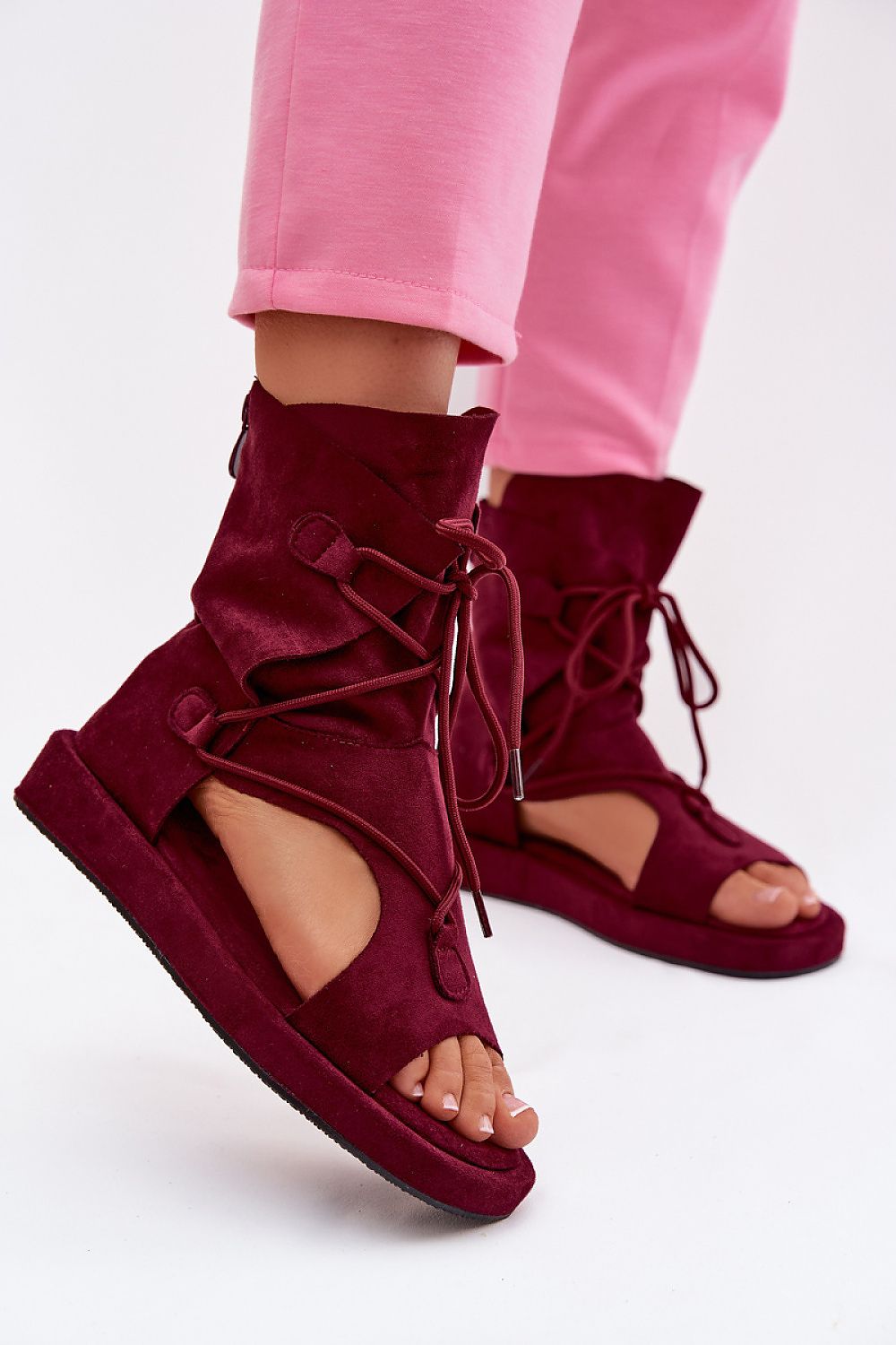 Burgundy open-toe sandals with lace-up design worn with pink pants on a white background