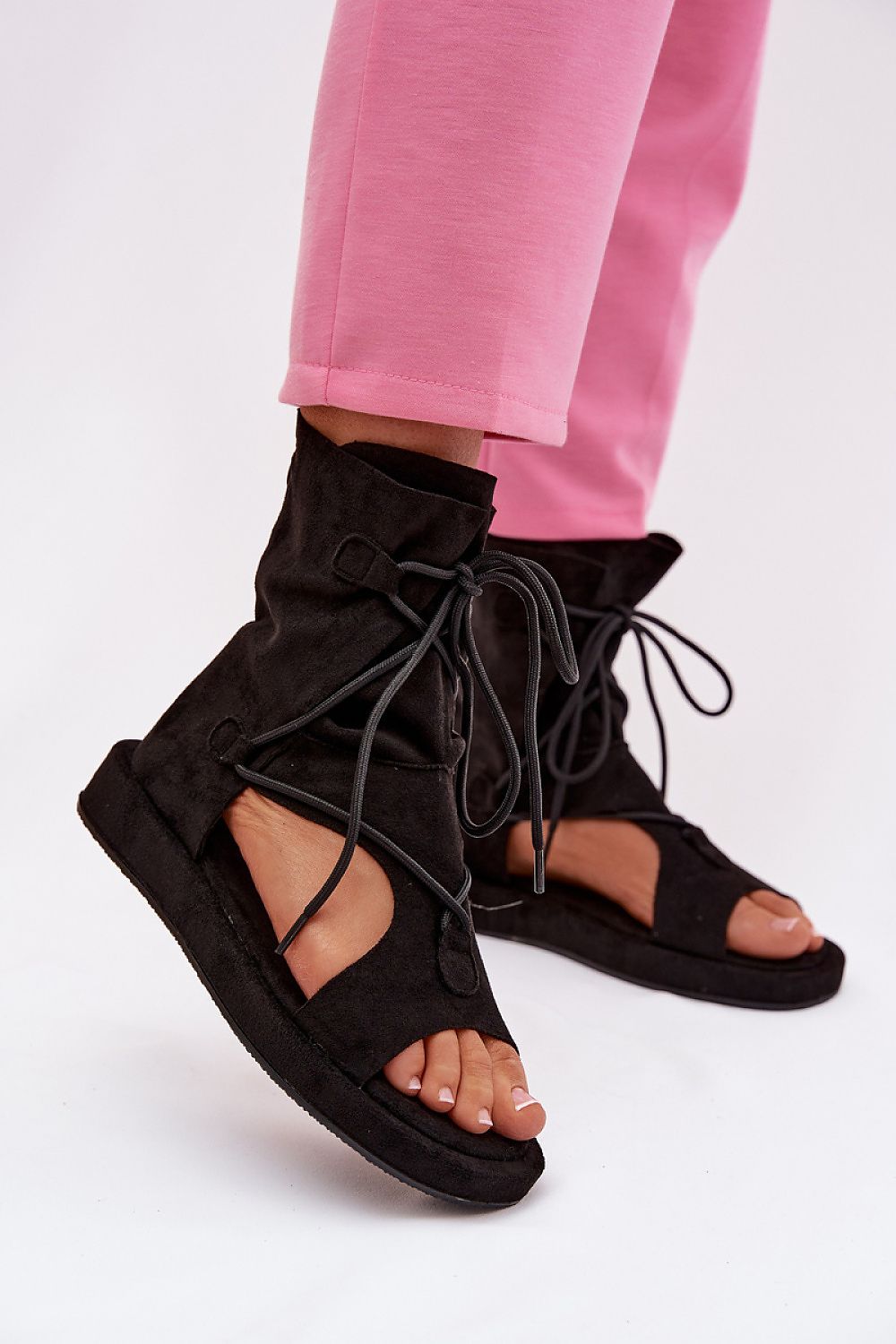 Black lace-up sandals worn with pink pants on a white background
