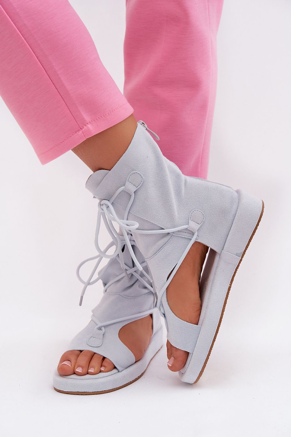 Light gray lace-up sandals worn with pink pants on a white background