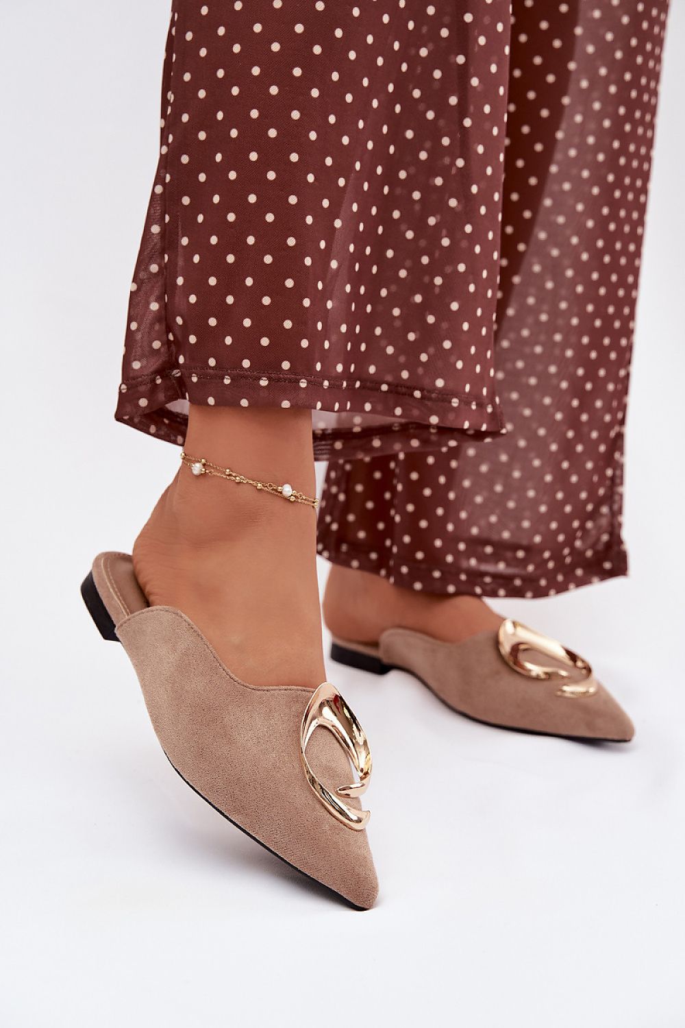 Beige pointed-toe shoes with gold accents worn with a brown polka dot dress.