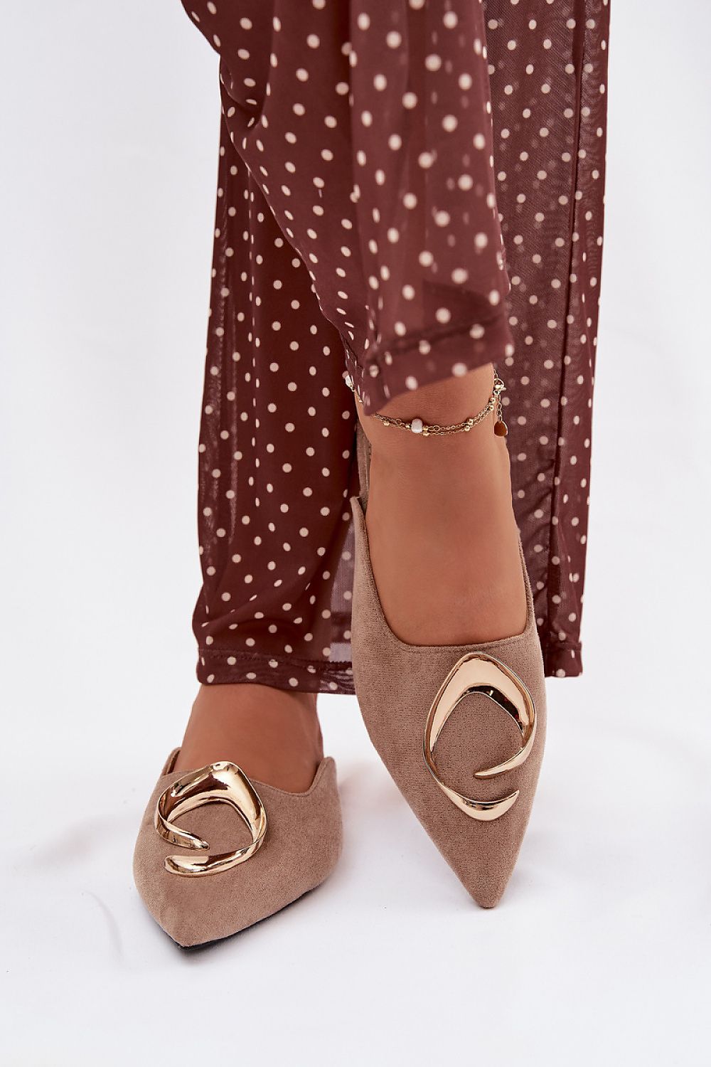 Brown suede shoes with gold buckles worn with polka dot pants on a white background