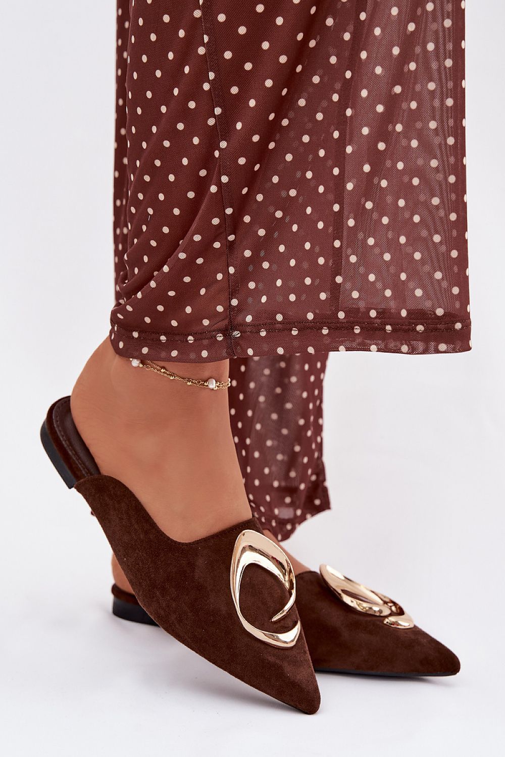 Brown suede shoes with gold accents worn with a brown polka dot dress on a white background