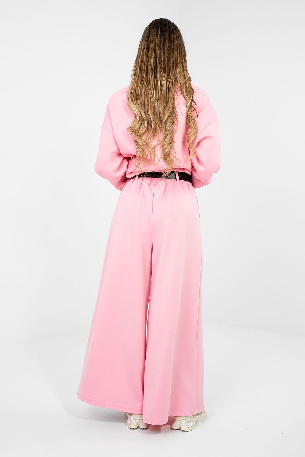 Person wearing a pink outfit with a long dress and jacket on a white background