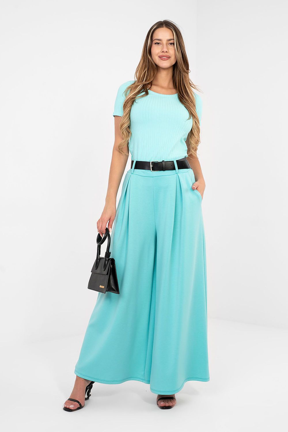 Woman wearing a light blue dress with a belt and holding a black handbag on a white background