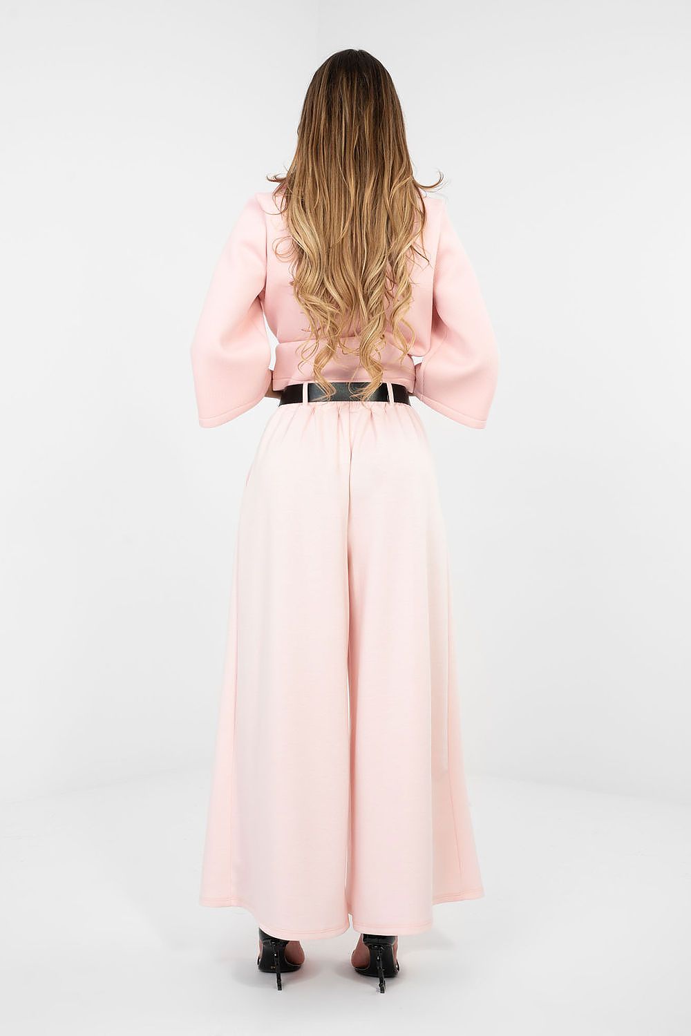 Woman wearing a long pink dress with a belt on a white background