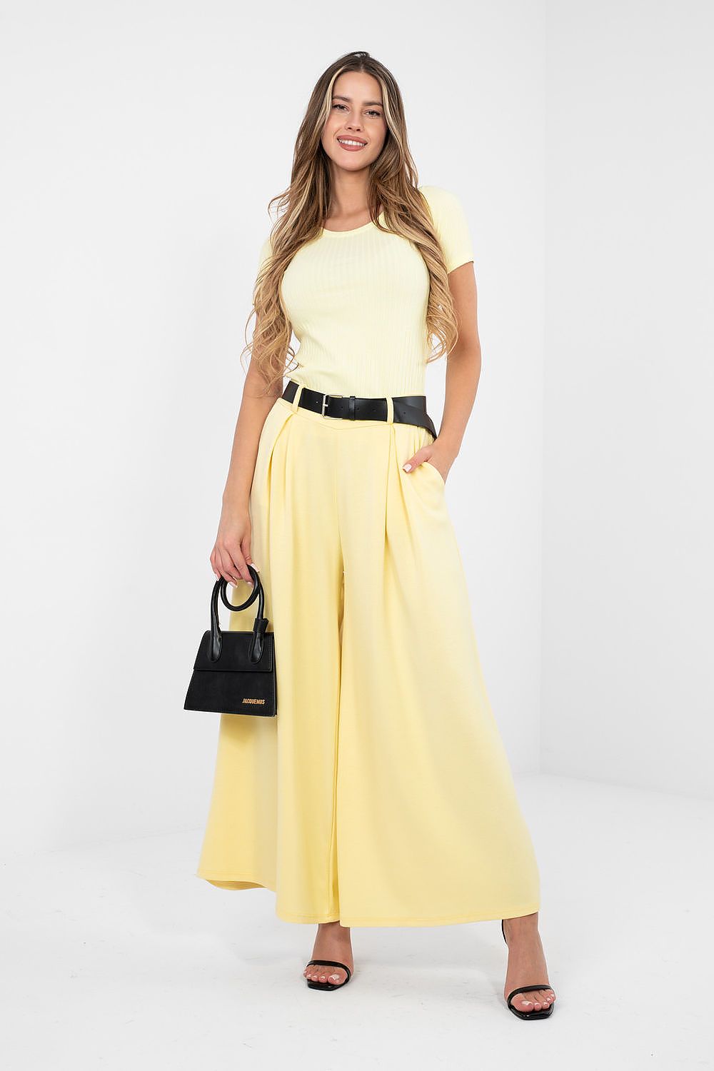 Woman wearing a yellow outfit with a black belt and handbag on a white background