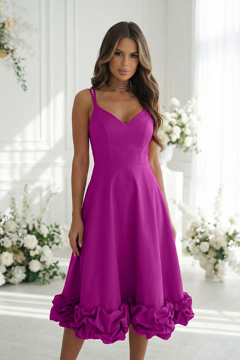 Woman wearing a purple dress with floral details in a bright room with flowers.