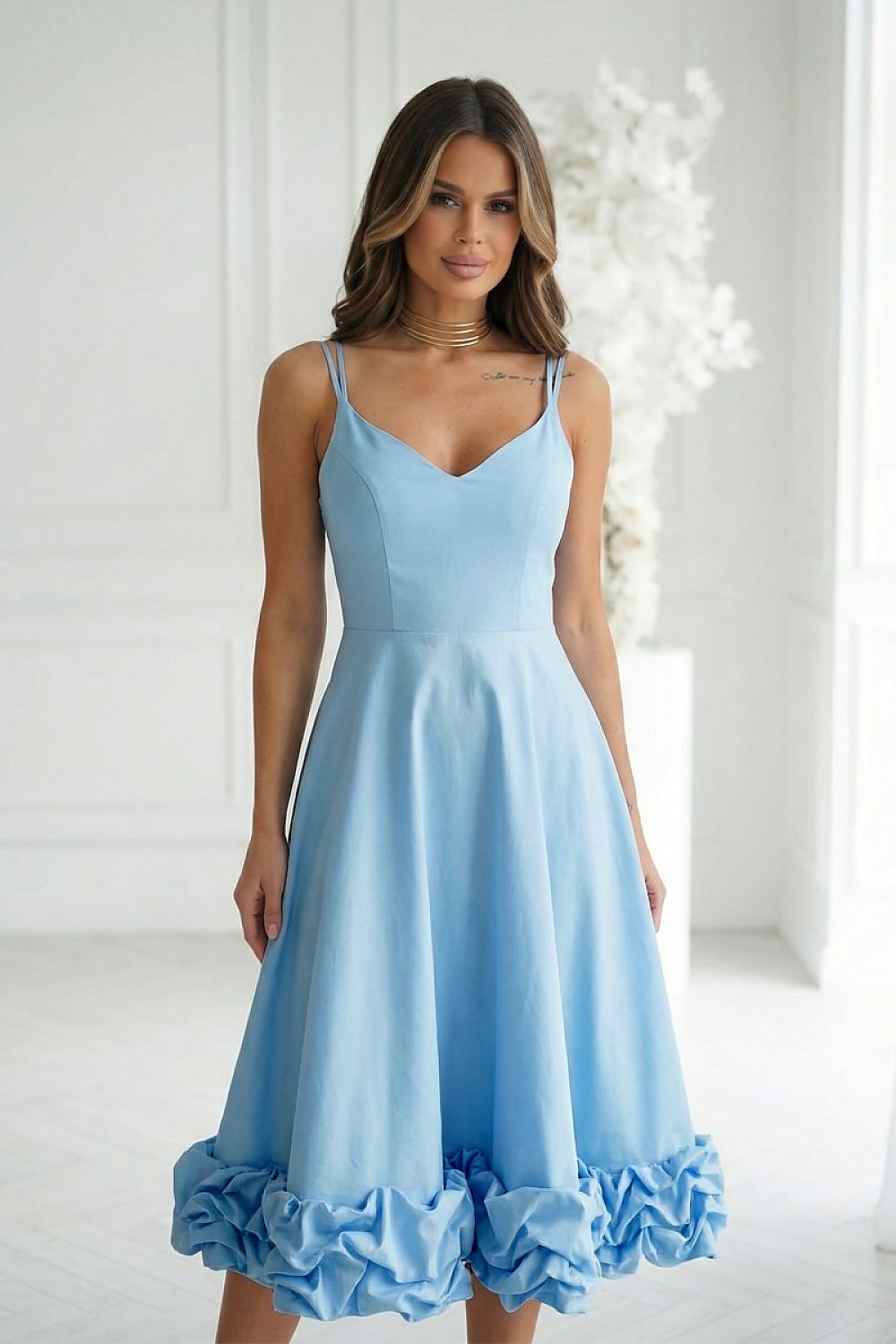 Woman wearing a light blue dress with ruffled hem in a bright room.
