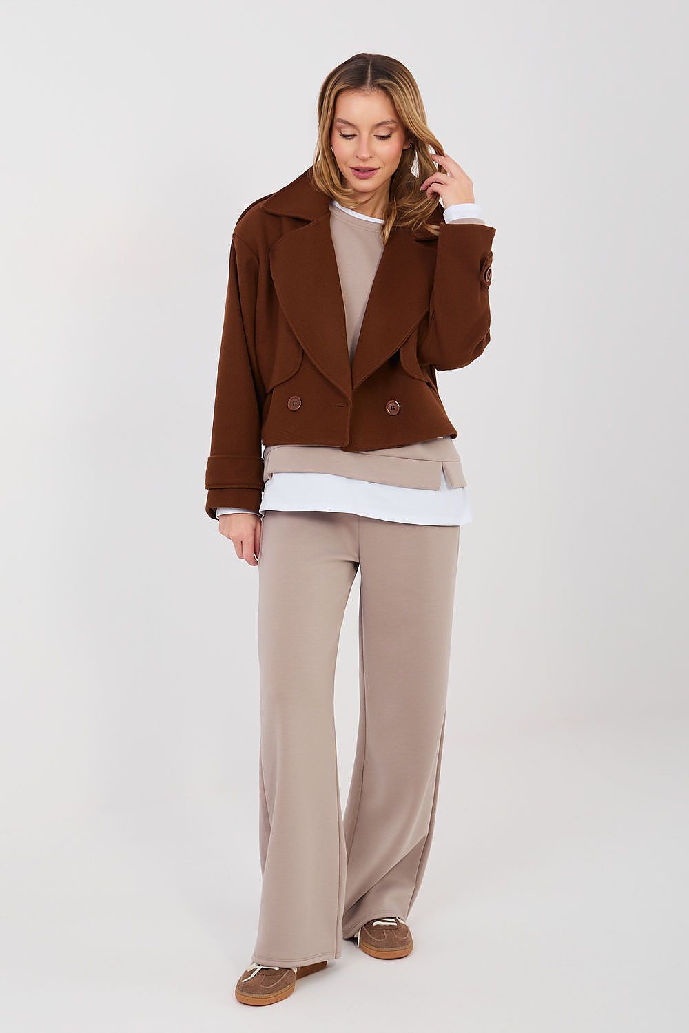 Woman wearing a brown jacket and beige pants on a white background