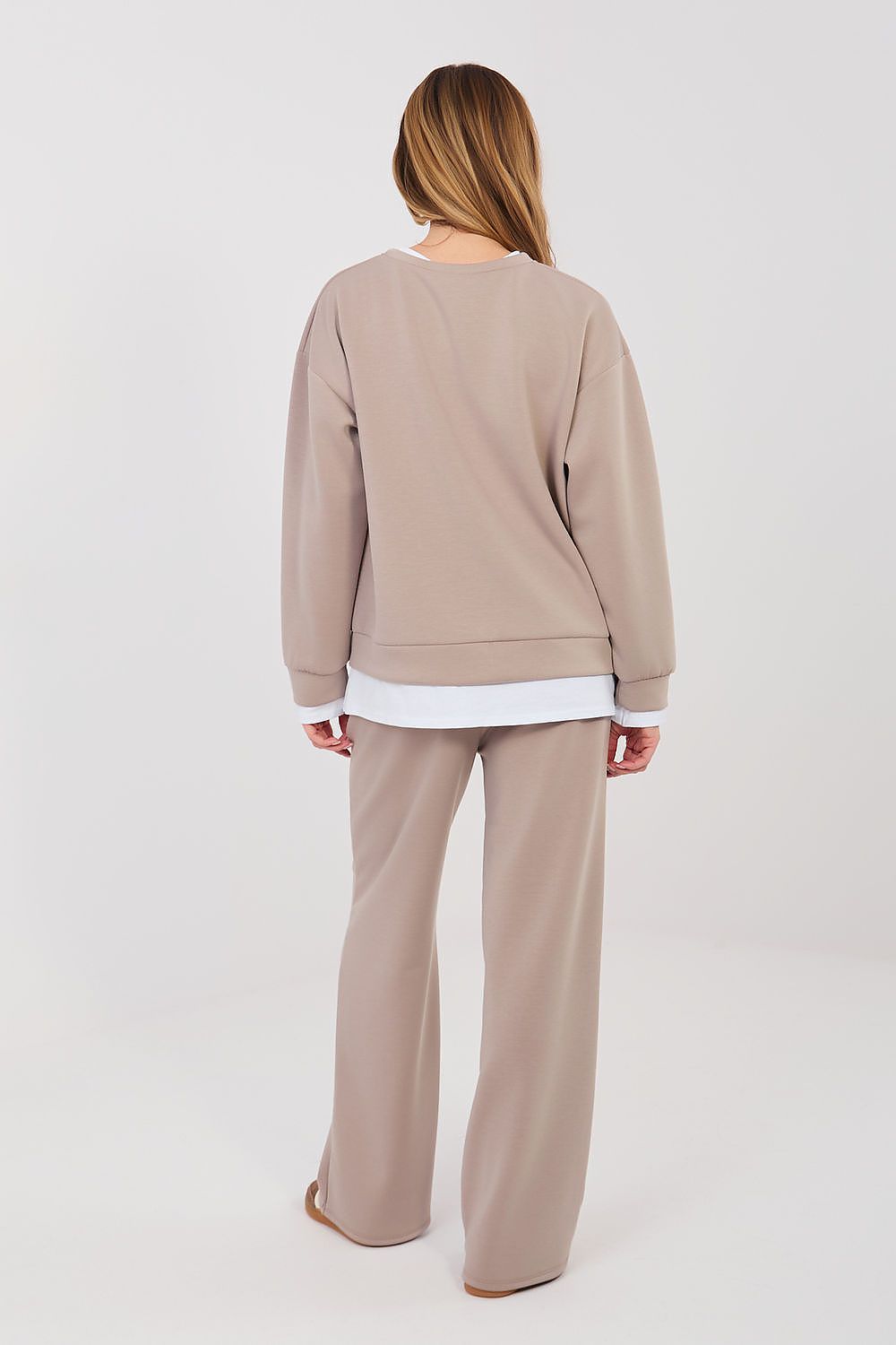 Person wearing a beige sweater and pants set on a white background