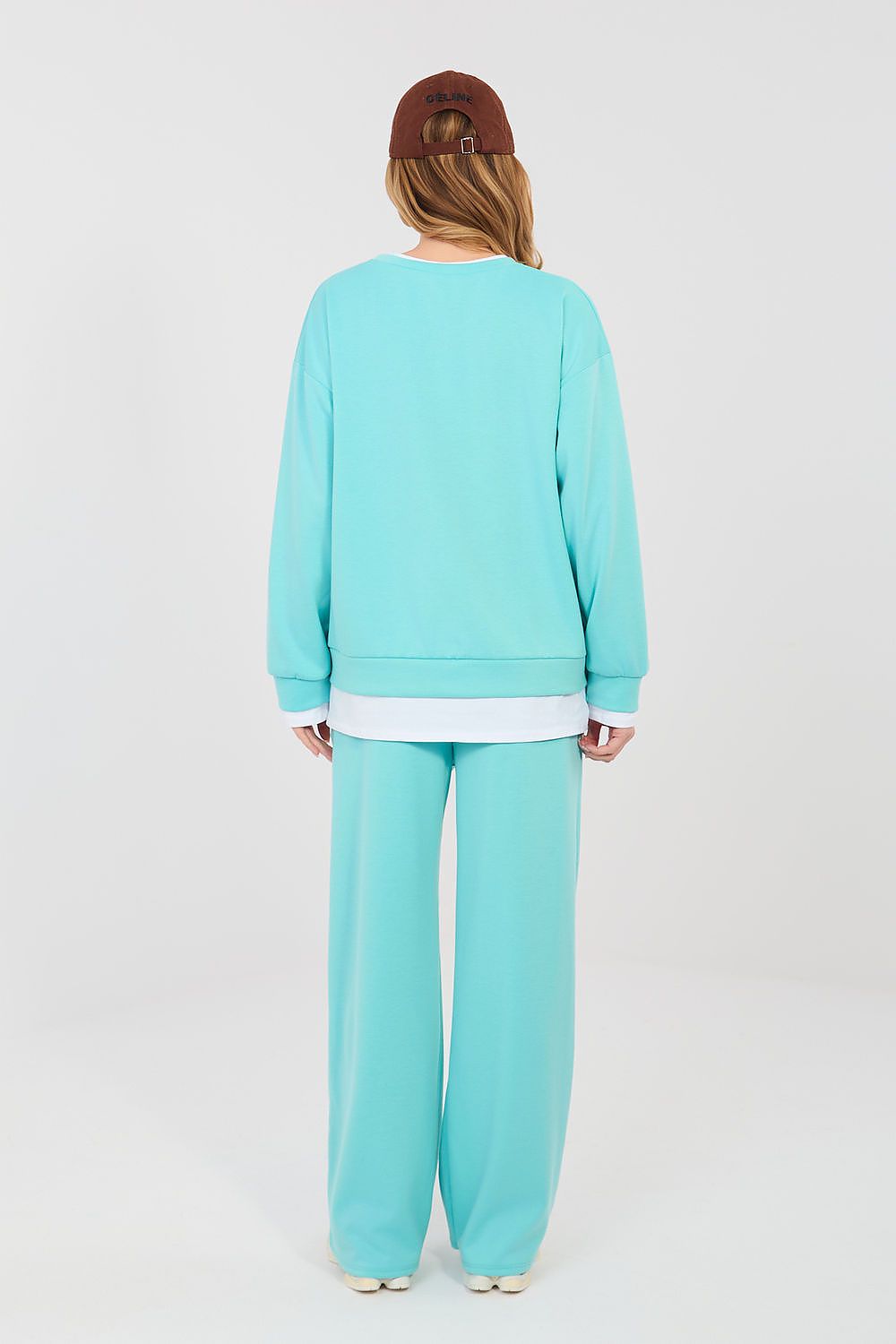 Person wearing a turquoise tracksuit and brown cap on a white background