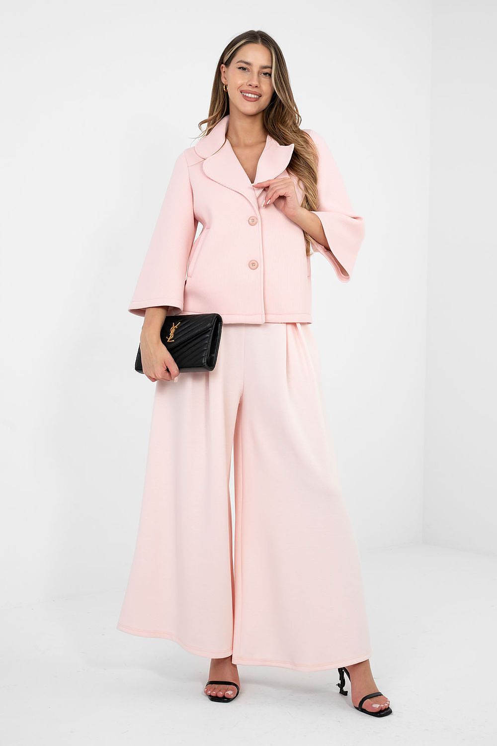 Woman wearing a pink suit with a black clutch against a white background